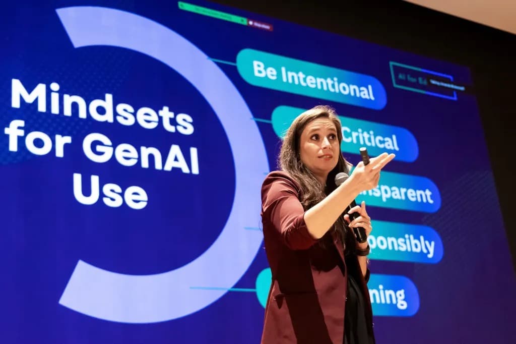 A woman presenting AI literacy guidelines on stage in front of a slide reading Mindsets for GenAI Use