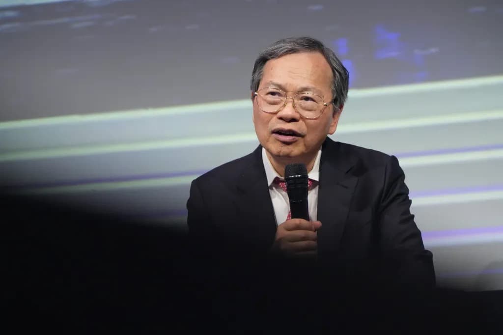 A man speaking into a microphone on stage in front of a large screen